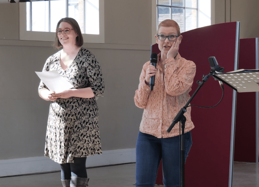 2 people one witha piece of paper, one with a microphone in hand